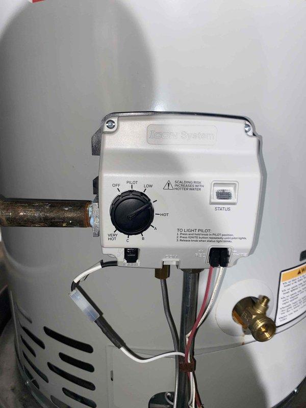 Responded to emergency no hot water call for 2-year-old tanked water heater. Upon inspection, found Honeywell Iicon System gas control valve in proper position but water heater failing to maintain temperature. Verified pilot light status, examined control settings ranging from OFF through PILOT, LOW, and HOT positions. Inspected gas supply lines, copper piping connections, and brass fittings for proper operation. Assessed venting system including PVC exhaust routing and clearances to adjacent HVAC equipment. Checked electrical connections including bundled black, white, and red wiring from control module. Evaluated installation compliance with manufacturer specifications visible on tank labels. Examined mounting straps, seismic restraints, and overall unit stability. Photographed gas control valve assembly and mechanical room configuration for service records. Restored hot water functionality and verified proper operation of heating system before departure.