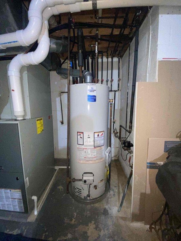 Responded to emergency no hot water call for 2-year-old tanked water heater. Upon inspection, found Honeywell Iicon System gas control valve in proper position but water heater failing to maintain temperature. Verified pilot light status, examined control settings ranging from OFF through PILOT, LOW, and HOT positions. Inspected gas supply lines, copper piping connections, and brass fittings for proper operation. Assessed venting system including PVC exhaust routing and clearances to adjacent HVAC equipment. Checked electrical connections including bundled black, white, and red wiring from control module. Evaluated installation compliance with manufacturer specifications visible on tank labels. Examined mounting straps, seismic restraints, and overall unit stability. Photographed gas control valve assembly and mechanical room configuration for service records. Restored hot water functionality and verified proper operation of heating system before departure.