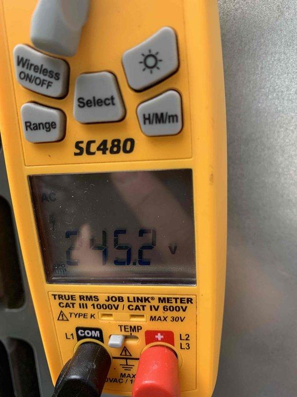 Completed routine AC maintenance and system diagnostics on outdoor condensing unit. Inspected condenser coil assembly, noting moderate dirt and debris accumulation between aluminum fins with some minor fin deformation present. Verified electrical operation with multimeter, recording 245.2 volts at unit, confirming proper power supply within acceptable range for equipment operation.