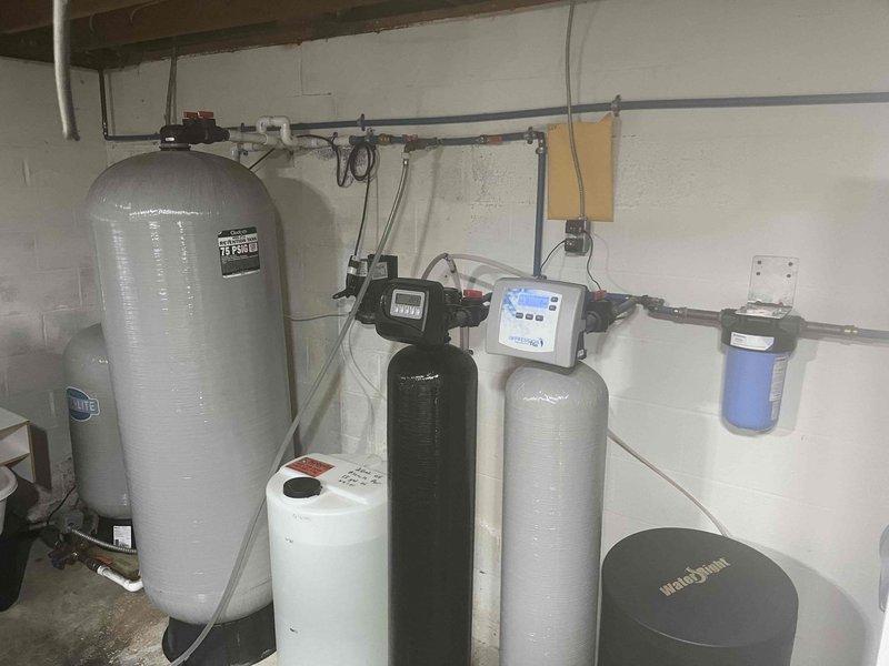 Responded to service call for odor issues in water supply caused by depleted chlorine injection system. Customer had already refilled the chlorine holding tank prior to arrival. Inspected existing water treatment system consisting of pressure tank, dual filtration tanks with digital controls, brine tank, and inline filter housing. Verified chlorine feed equipment was operational following tank refill and confirmed proper system function to restore water quality.