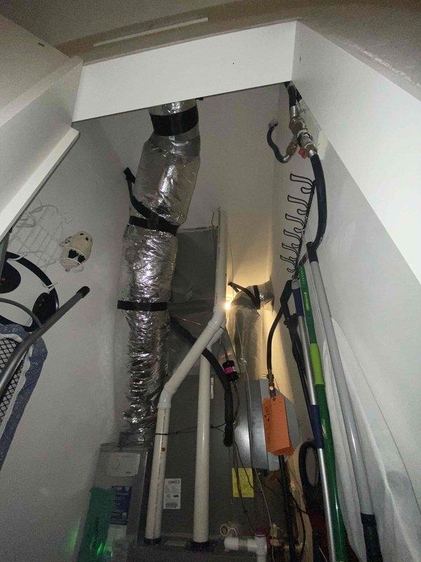Completed on-site evaluation for furnace replacement system in residential property. Assessed existing HVAC infrastructure including vertical ductwork configuration in confined utility closet space, examined outdoor condenser unit positioning relative to building exterior, and documented current system layout with white PVC condensate drainage lines and electrical connections. Provided comprehensive replacement estimate for furnace-only upgrade while noting adequate clearance requirements around exterior equipment currently obscured by landscaping vegetation.