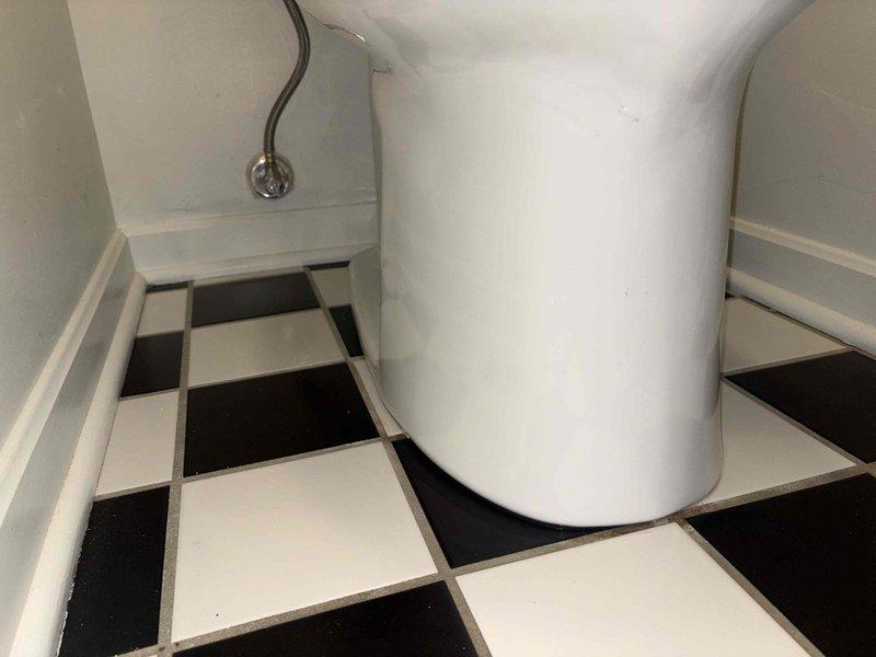 Completed toilet replacement in bathroom with classic checkerboard tile flooring. Removed existing fixture and installed new white porcelain toilet, connecting braided stainless steel supply line to chrome shut-off valve with proper sealing and secure mounting to ensure leak-free operation.