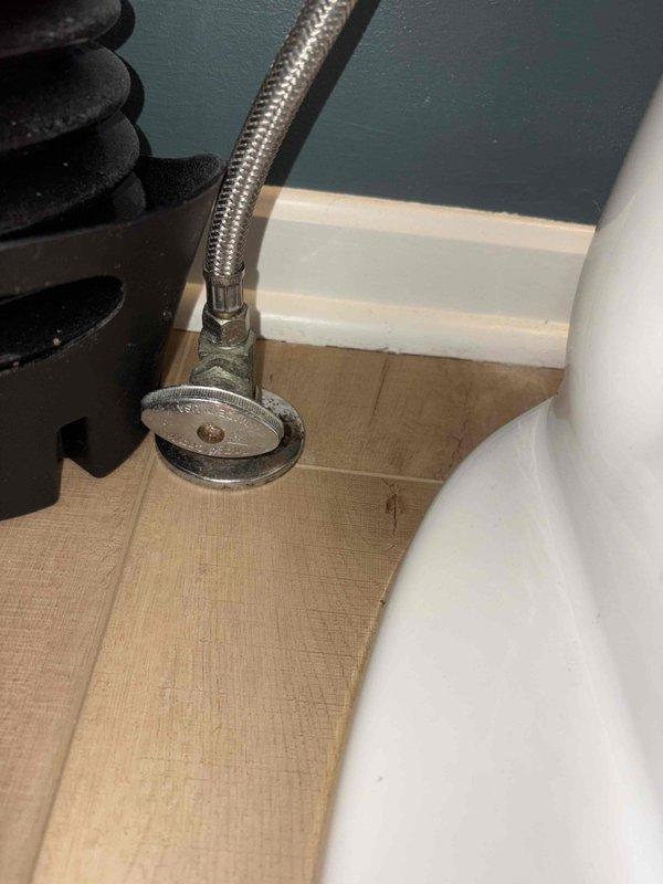 Completed toilet replacement in bathroom with classic checkerboard tile flooring. Removed existing fixture and installed new white porcelain toilet, connecting braided stainless steel supply line to chrome shut-off valve with proper sealing and secure mounting to ensure leak-free operation.