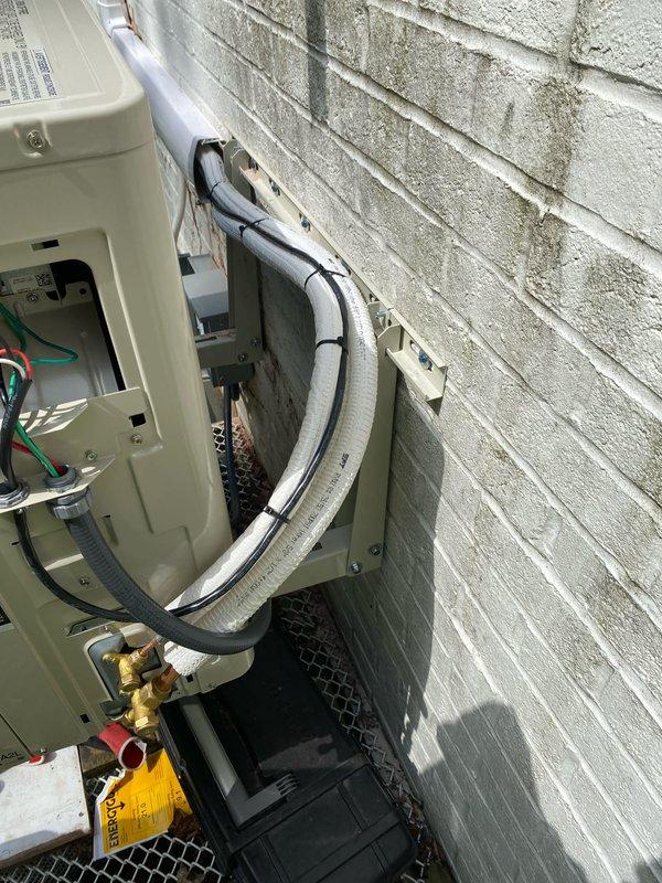 Completed mini-split system installation with outdoor condensing unit mounted on exterior brick wall and indoor air handler installed on interior wall. Ran and insulated refrigerant line set between units, installed electrical disconnect box with proper wiring and grounding, secured all connections at service valves, and verified level placement of indoor unit using precision leveling tools.