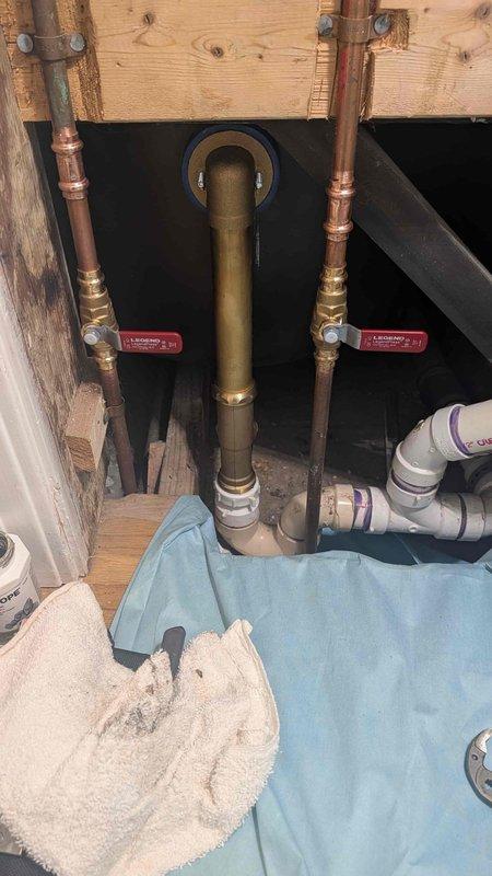 Completed installation of bathtub waste and overflow assembly along with exterior hose bib replacement. Installed new dual-handle hose bib with brass valve body and separate hot/cold water controls mounted to exterior brick wall, with proper shut-off valves on copper supply lines. Replaced tub waste and overflow system including drain assembly with blue rubber boot seal at floor penetration and PVC drain connections beneath the fixture. All connections tested and verified leak-free upon completion.