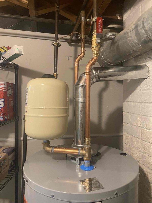 Responded to service call for 40-gallon gas water heater with leak at base of tank where bottom attaches to footer assembly. Upon inspection, confirmed active leak originating from lower tank seam, indicating internal tank failure. Documented existing installation including standard atmospheric venting, copper supply lines, expansion tank, pressure relief valve, and associated plumbing connections for replacement specifications.