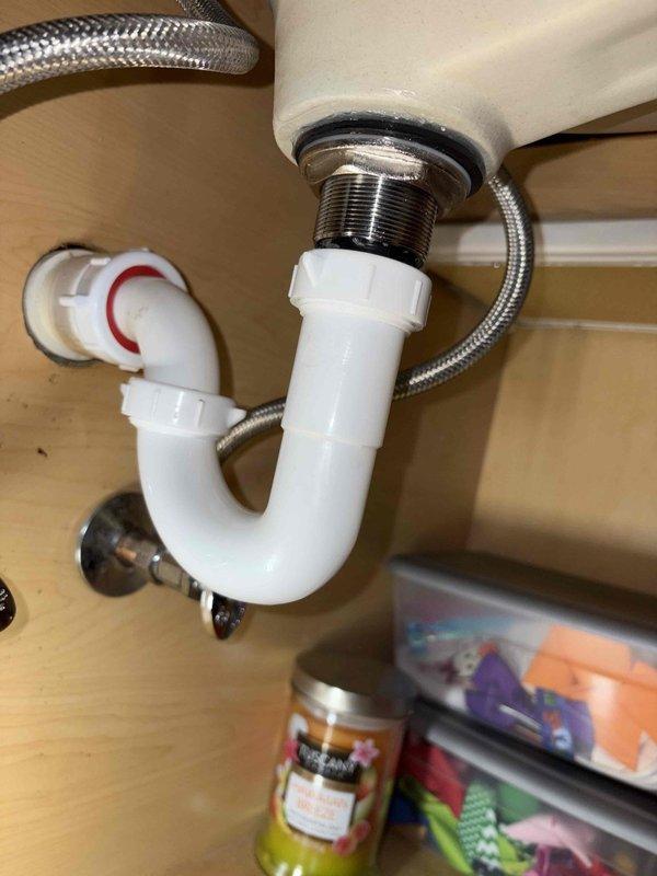 Responded to emergency call for major plumbing leak in approximately twenty-year-old residential property. Upon inspection, identified leak source at sink drain assembly and water heater control system. Inspected under-sink plumbing connections including P-trap, chrome tailpiece with rubber gasket and locknut, and braided stainless steel supply lines. All connections appeared secure with no visible signs of deterioration at basin drain assembly.

Examined water heater Icon System control unit, noting ON/OFF rocker switch and temperature dial with settings ranging from standard to very hot positions. Inspected brass valve connections and associated white tubing beneath control panel. Traced leak to compromised connection point requiring adjustment and resealing. Tightened all accessible fittings, verified proper gasket placement, and tested system integrity under normal operating pressure.

Documented conditions with photographic evidence showing plumbing components, control systems, an