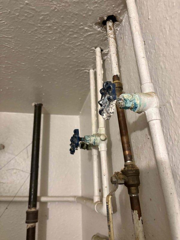Conducted comprehensive HVAC system evaluation for complete replacement estimate on existing Rheem outdoor condensing unit. Assessed current equipment condition including weathered refrigerant line insulation, aged copper piping connections, and electrical disconnect configuration. Documented exterior condenser placement on concrete pad with overgrown vegetation clearance concerns. Evaluated interior plumbing infrastructure including water supply lines, shut-off valves, and copper piping showing corrosion and mineral buildup at connection points. Provided detailed photographic documentation of all system components to support replacement recommendations and equipment specifications.