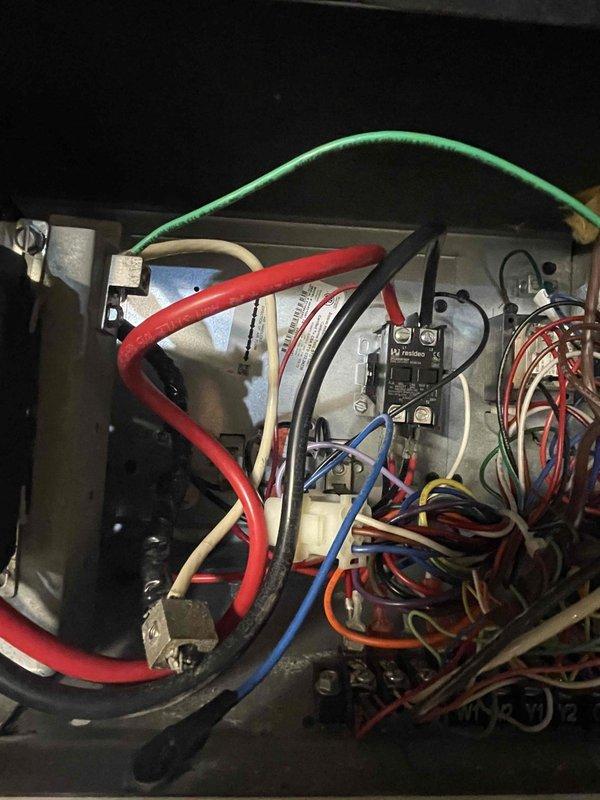 Responded to return service call for heat pump failure affecting entire home approximately 2-2.5 weeks after previous repair of burnt wire at outdoor unit. Upon arrival, inspected indoor air handler unit in basement and outdoor heat pump system. Examined electrical control panel and contactor assembly based on customer concern of unresolved issue with indoor unit. Found Resideo contactor and associated wiring connections in electrical junction box. Evaluated all wire terminations including red, blue, white, pink, yellow, green, and black conductors at contactor terminals. Inspected previous repair work on outdoor unit wiring. Tested contactor operation and verified proper electrical connections throughout control circuit. Reviewed system operation under warranty coverage. Documented electrical panel configuration and contactor assembly with photographs showing wire routing, terminal connections, and component mounting. System restored to operational status with whole-house heating capa
