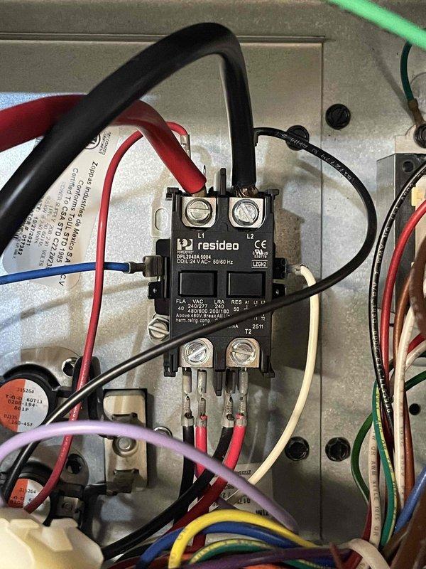 Responded to return service call for heat pump failure affecting entire home approximately 2-2.5 weeks after previous repair of burnt wire at outdoor unit. Upon arrival, inspected indoor air handler unit in basement and outdoor heat pump system. Examined electrical control panel and contactor assembly based on customer concern of unresolved issue with indoor unit. Found Resideo contactor and associated wiring connections in electrical junction box. Evaluated all wire terminations including red, blue, white, pink, yellow, green, and black conductors at contactor terminals. Inspected previous repair work on outdoor unit wiring. Tested contactor operation and verified proper electrical connections throughout control circuit. Reviewed system operation under warranty coverage. Documented electrical panel configuration and contactor assembly with photographs showing wire routing, terminal connections, and component mounting. System restored to operational status with whole-house heating capa