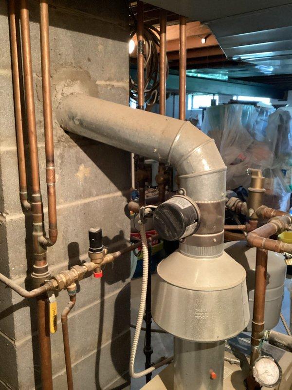 Completed HVAC estimate for boiler replacement due to active leak in existing unit. Assessed basement mechanical room containing aging boiler system with associated plumbing infrastructure, humidifier components, and copper piping network. Documented existing equipment configuration including water heater installed in 2014, multiple shut-off valves, and ductwork connections. Photographed current system layout showing concrete block walls, exposed floor joists, and utility connections to provide comprehensive replacement proposal. Identified need to coordinate sump pump relocation in conjunction with new boiler installation.