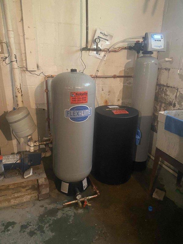 Responded to service call for malfunctioning water softener system. Upon arrival, inspected complete water treatment setup including Flex-Lite pressure tank, water softener with digital control head, expansion tank, and associated copper piping and brass valve assemblies. Diagnosed water softener control head failure preventing proper regeneration cycle. Assessed condition of all equipment and plumbing connections, noting significant floor staining indicating past water issues. Presented property representative with repair versus replacement options for approval, including cost analysis for new water softener installation versus control head replacement on existing unit.