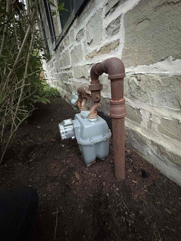 Responded to emergency call for reported gas odor detected both inside and outside the property near the meter area of a 1952-built residence. Upon arrival, conducted thorough visual inspection of gas system components including interior piping and exterior meter assembly. Documented extensive corrosion and deterioration on metal gas piping throughout the system, particularly noting severe rust accumulation on interior vertical gas line running from ceiling to floor level with significant oxidation at base connections and wall penetration points. Exterior inspection revealed gas meter installation with heavily corroded brown metal piping showing advanced rust deterioration on all exposed surfaces and fittings. Performed comprehensive gas leak detection testing using appropriate detection equipment to identify source of reported odor. Evaluated structural integrity of aging gas distribution system and assessed safety concerns related to corroded piping condition. Provided recommendation