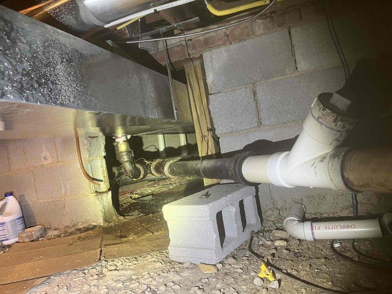# Plumbing Service Completed

Responded to service call for gurgling sounds occurring in kitchen sinks during water usage. Upon investigation, accessed crawl space beneath the building to inspect the drainage system. Discovered severely corroded drain pipes showing extensive rust, surface degradation, and material deterioration on the main waste line. The corroded metal piping exhibited significant pitting and flaking, particularly on the horizontal drain run connecting to the kitchen sink system.

Documented the condition of the deteriorating pipe infrastructure, noting the transition point where newer white PVC piping connects to the older corroded metal sections. The severe corrosion on the main drain line was identified as the likely cause of restricted water flow and improper venting, resulting in the gurgling sounds reported by the customer. The deteriorated pipe surface and internal buildup can create air pressure imbalances within the drain system, producing characteristic gurg