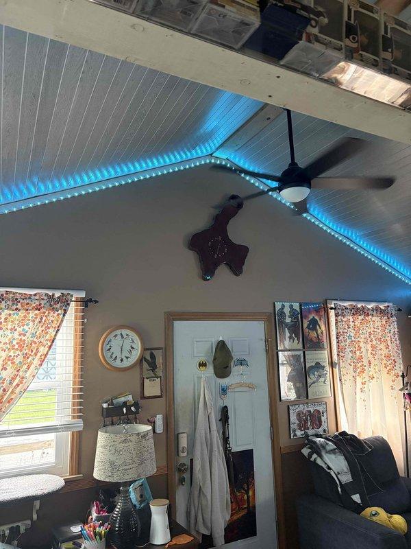 Conducted on-site evaluation for mini split installation in main living area featuring vaulted ceiling with exposed beams and ceiling fan. Assessed interior space dimensions, electrical access points, and optimal indoor unit placement to accommodate existing ceiling architecture and lighting fixtures. Evaluated exterior wall access and staging area for outdoor condenser unit placement, noting proximity to existing fence line and available mounting locations on pale yellow siding beneath covered overhang.