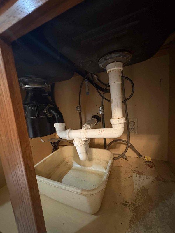 Removed non-functional garbage disposal unit from under-sink cabinet and reconfigured plumbing to standard drain configuration. Disconnected electrical supply and mounting hardware from disposal, capped electrical connection per code, and installed new PVC P-trap assembly with proper venting to restore full drainage capability to sink basin.