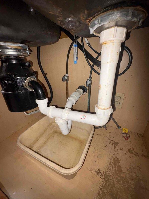 Removed non-functional garbage disposal unit from under-sink cabinet and reconfigured plumbing to standard drain configuration. Disconnected electrical supply and mounting hardware from disposal, capped electrical connection per code, and installed new PVC P-trap assembly with proper venting to restore full drainage capability to sink basin.
