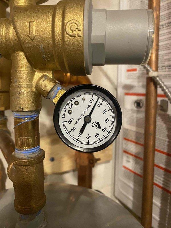 Responded to service call for leaking two-year-old combi boiler that had lost approximately one gallon of water over the weekend. Upon inspection, identified leak at coupler connection to filter assembly and verified system pressure readings on gauge. Examined brass valve manifold, circulator pump, and associated copper piping connections for additional leak points. Documented plumbing configuration including pressure gauge assembly, shut-off valves, and circulator pump operation to assess system integrity and pressure regulation.