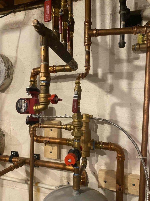 Responded to service call for leaking two-year-old combi boiler that had lost approximately one gallon of water over the weekend. Upon inspection, identified leak at coupler connection to filter assembly and verified system pressure readings on gauge. Examined brass valve manifold, circulator pump, and associated copper piping connections for additional leak points. Documented plumbing configuration including pressure gauge assembly, shut-off valves, and circulator pump operation to assess system integrity and pressure regulation.