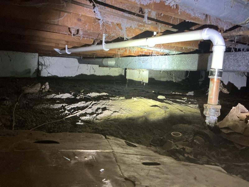 Completed comprehensive plumbing inspection and documentation of crawl space drainage system beneath residential structure. Inspected and photographed existing PVC drain line configuration including multiple P-trap assemblies, horizontal drain runs, and connection points to verify proper installation and identify any repairs needed per previous service agreement. All plumbing components, structural supports, and foundation access areas were examined and documented for service records.