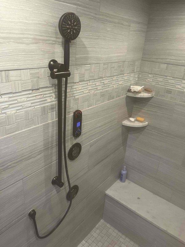 Responded to service call for detached shower head tubing. Upon inspection, found the handheld shower hose had separated from the mounting connection point on the slide bar assembly. Reattached and secured the flexible hose connection to the bronze finish slide bar system, ensuring proper threading and seal integrity. Tested water flow through both the overhead shower head and handheld unit to verify no leaks at connection points and confirm full functionality of the dual shower system.