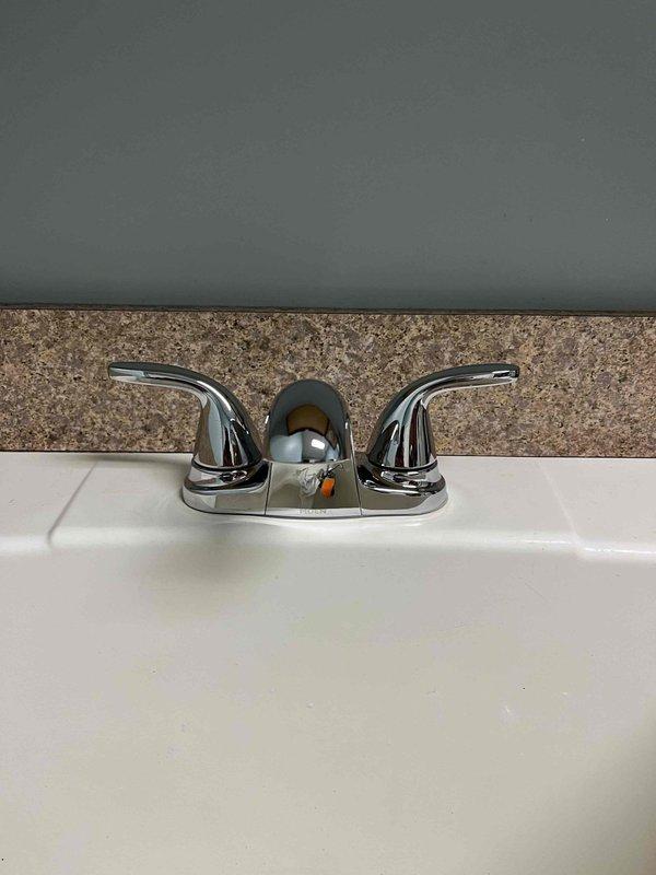 Completed replacement of two faucets in the residence: a chrome two-handle bathroom faucet with lever-style handles and lift rod assembly installed on a white ceramic sink, and an oil-rubbed bronze single-handle kitchen faucet with matching soap dispenser installed on granite countertop above an undermount sink. Both fixtures were properly mounted, connected to supply lines, tested for proper operation and leaks, with all components functioning correctly upon completion.