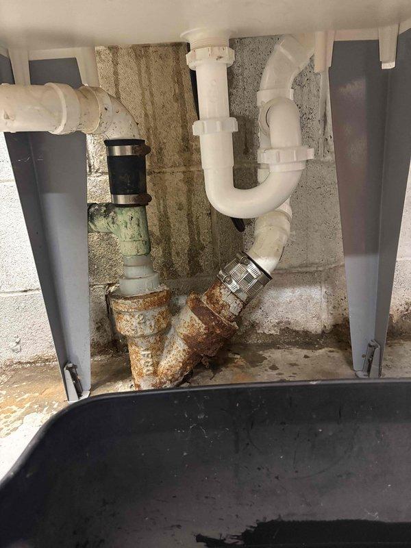 Responded to callback regarding exterior hose bibs dispensing hot water and persistent cloudy water condition one month after new water treatment system installation. Upon inspection, discovered cross-connection issue affecting outdoor faucets, causing hot water supply to both exterior fixtures. Investigated utility sink plumbing assembly where corroded galvanized piping beneath basin was identified as contributing factor to water discoloration. The heavily rusted metal pipes showed significant oxidation that could be introducing sediment into the water system. Assessed P-trap assembly and drainage components above the corroded section. Documented condition of existing plumbing infrastructure showing deteriorated metal piping requiring replacement to resolve ongoing water quality issues. Advised that foggy water appearance after one month indicates either inadequate system flushing following installation or continued contamination from degraded pipe interiors. Recommended complete repl