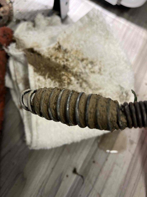 Responded to backup issue in basement of 73-year-old residential property. Upon inspection, found severely corroded plumbing components including deteriorated metal flange at pipe penetration point and heavily corroded drain line coil/spring mechanism. Deployed powered drain auger to clear blockage in main basement drain line. Successfully removed obstruction and restored proper drainage flow. Documented existing corrosion on vintage plumbing infrastructure for homeowner's awareness regarding future maintenance needs.