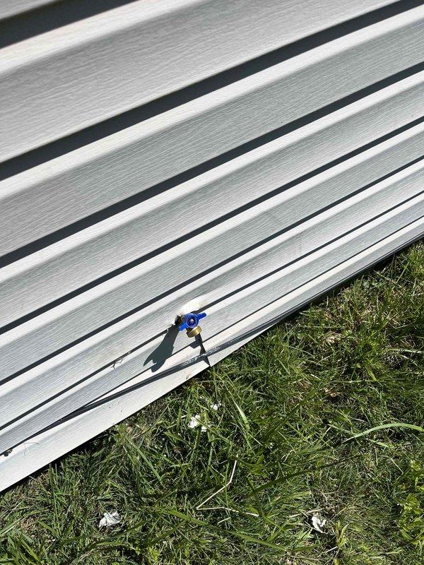 Installed outdoor hose bib with blue handle on exterior wall between two downspouts as part of promotional buy-one-get-one spigot offer. Completed installation on white vinyl siding with proper mounting and verified operational functionality of the new water spigot.
