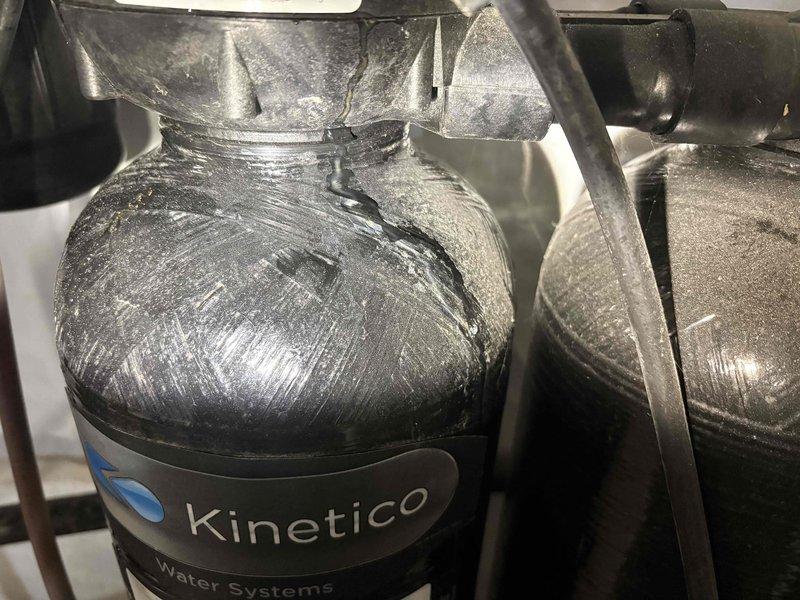 Replaced filter on Kinetico water softening system and performed inspection of boiler system. During service, baseboard heating system required draining due to pressure issues. Following filter replacement, discovered active water leak at discharge tube connection leading to sump pump. Leak was identified after toilet flush test revealed loud noise and water overflow. Documented rust staining and mineral deposits on system components. Additional boiler-related concerns noted for follow-up evaluation.