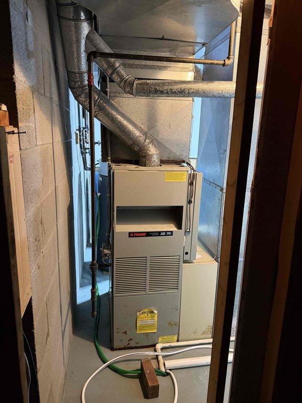 Conducted comprehensive assessment of existing residential HVAC system for replacement estimate. System consists of Trane XR 70 furnace located in basement utility area and corresponding outdoor air conditioning unit mounted on concrete blocks adjacent to building exterior. Documented current equipment configuration including ductwork connections, electrical disconnect, refrigerant lines, and condensate drainage system. Captured detailed photographic documentation of both indoor and outdoor units to support replacement options and equipment specifications.