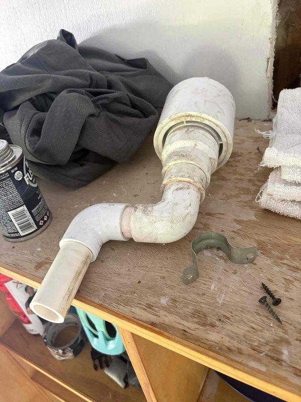 Returned to property to reconnect furnace condensate drain line to original configuration following previous water damage incident. Accessed repair area through existing drywall openings in wall and ceiling that exposed internal structure and PVC drainage system. Reassembled white PVC condensate drain piping using elbow fittings to restore proper drainage path from furnace unit. Performed operational test by running water through drain line to verify proper flow and confirm system functionality with no leaks or blockages detected. Evidence of previous water damage and moisture infiltration visible on wooden framing and floor surfaces in affected area.