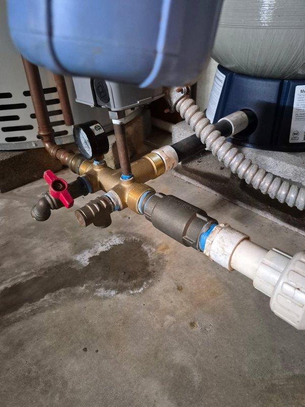 Responded to water leak complaint and inspected plumbing manifold assembly beneath water heater system. Found brass manifold fitting with visible crack causing active leak onto concrete floor. Replaced damaged manifold component and associated fittings, ensuring proper seal on all copper pipe connections. Tested system under full pressure to verify leak repair was successful with no further water discharge observed.