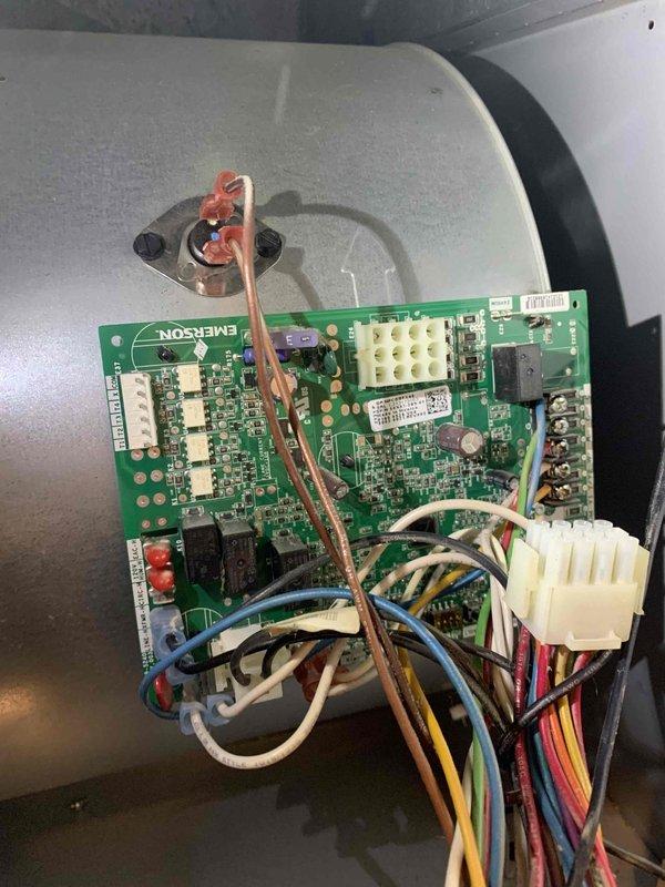 Returned to property to replace defective control board under warranty. Removed access panel to HVAC unit and disconnected existing Emerson control board, carefully detaching all wire harness connections from the multi-pin connectors. Installed new replacement control board, reconnected all wiring including white, blue, brown, yellow, red, pink, and black wires to proper terminals, and secured board in enclosure. Verified all connections were tight and properly seated, reinstalled access panel, and tested system operation to confirm successful repair.
