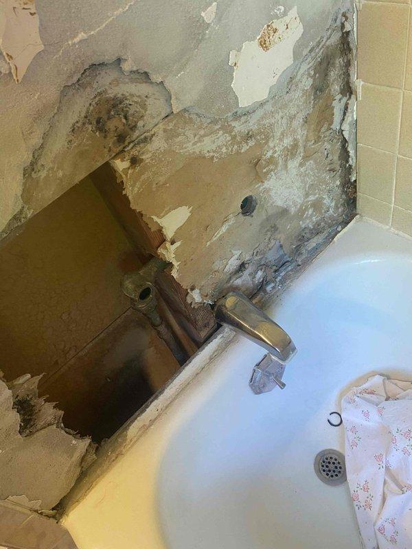 Responded to address multiple plumbing concerns in bathroom with water damage from previous leak. Permanently repaired temporary copper hot water pipe fix that had been improperly addressed. Installed customer-supplied lavatory faucet and shower valve, adding two new shutoff valves to isolate bathroom plumbing system during shower valve installation. Work required accessing basement ceiling area where copper and PVC supply lines were visible among exposed wooden beams showing moisture damage. Bathroom walls exhibited significant deterioration and water staining around tub surround, indicating extent of previous leak damage. All installations completed using stock materials with proper isolation valves for future maintenance accessibility.