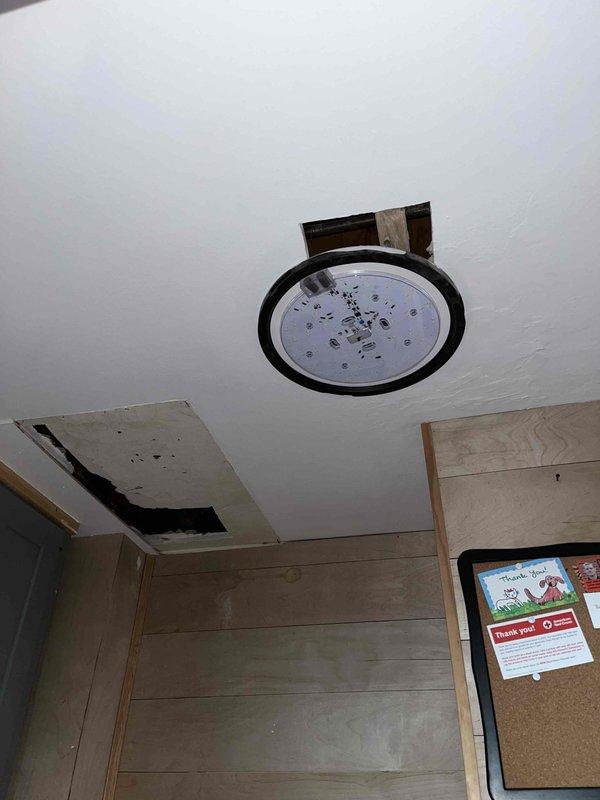 Responded to water leak emergency originating from shower penetrating through ceiling into living space below. Upon arrival, accessed crawl space above affected area to locate source of leak. Inspection revealed copper supply lines running through floor joists serving shower fixture. Identified active leak at connection point causing water damage to ceiling drywall and light fixture assembly. Removed damaged ceiling section to assess extent of water intrusion and verify structural integrity of wooden framing. Repaired compromised pipe connection, tested system under pressure to confirm leak resolution, and documented pre-repair conditions showing water-damaged ceiling with exposed electrical junction box and missing drywall panel.