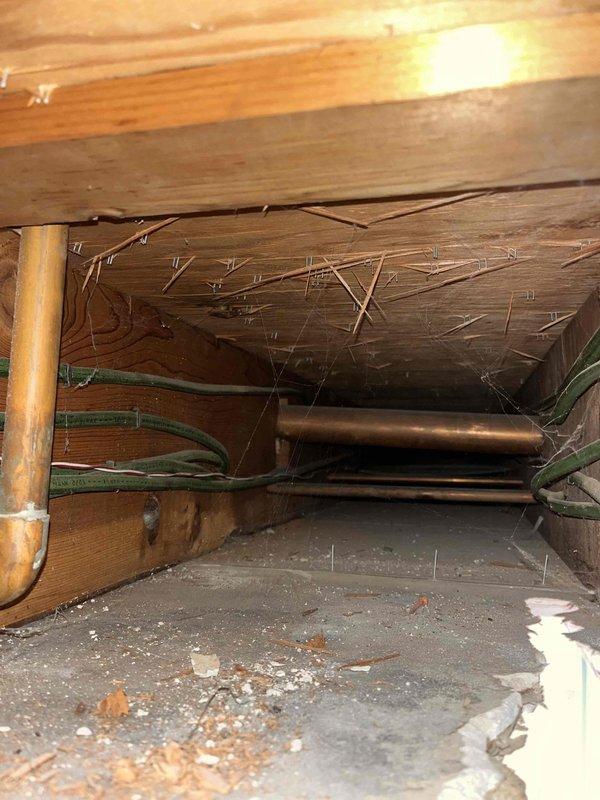 Responded to water leak emergency originating from shower penetrating through ceiling into living space below. Upon arrival, accessed crawl space above affected area to locate source of leak. Inspection revealed copper supply lines running through floor joists serving shower fixture. Identified active leak at connection point causing water damage to ceiling drywall and light fixture assembly. Removed damaged ceiling section to assess extent of water intrusion and verify structural integrity of wooden framing. Repaired compromised pipe connection, tested system under pressure to confirm leak resolution, and documented pre-repair conditions showing water-damaged ceiling with exposed electrical junction box and missing drywall panel.
