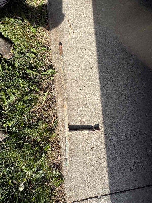 Returned to property to complete follow-up work on previously sold plumbing repair. Conducted thorough inspection of outdoor water service line area along concrete curb and property perimeter. Located and identified corroded metal stake marking the main water line shut-off valve position. Documented existing conditions showing significant oxidation and deterioration of the marker stake, which had developed green patina and rust damage affecting its visibility and structural integrity. Cleared vegetation and debris from the curb line to improve access to the water service area for future maintenance needs. Verified proper location of underground utilities and ensured all markers remained visible for emergency shut-off access.