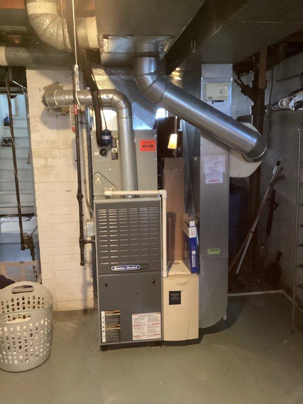 Conducted comprehensive assessment of existing HVAC system in residential basement mechanical room to provide replacement estimate for furnace and air conditioning equipment. Evaluated current American Standard furnace installation, associated ductwork configuration, and cooling system components. Documented existing equipment specifications, duct connections, electrical requirements, and spatial constraints for proper system replacement planning. Photographed current installation showing vertical furnace unit with metallic supply ductwork, humidifier integration, and electrical panel connections to ensure accurate equipment sizing and replacement specifications for both heating and cooling systems.