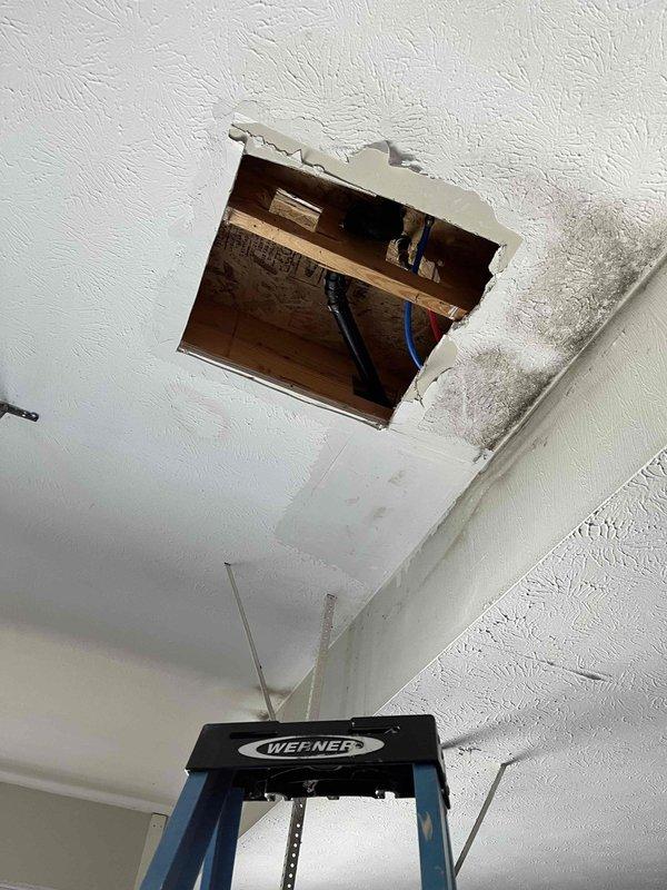 Responded to plumbing leak at supply line connection. Accessed piping through existing ceiling access panel using ladder. Located leak at threaded valve assembly where PEX supply lines (hot and cold) penetrate floor joists. Inspected flexible plastic supply lines and black threaded fitting mounted through subfloor. Repaired leaking connection at valve assembly to resolve recurring leak issue. Verified proper connection of pink hot water line and blue cold water line at penetration point. Restored system to proper working condition.