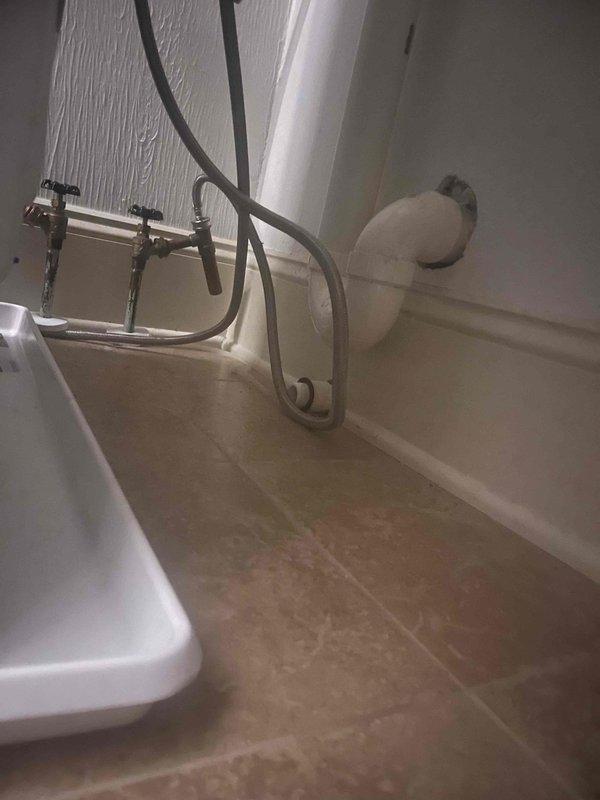 Replaced faulty washing machine shut-off valve in laundry room utility area. The original valve was incorrectly installed and required removal and replacement with proper chrome lever-handle shut-off valve to restore safe water supply connection to the washing machine.