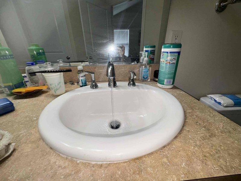 Completed follow-up plumbing repair service for bathroom vanity installation. Installed new three-piece chrome faucet set with separate hot and cold water handles and central spout on white oval drop-in sink with tan speckled countertop. All fixtures tested and confirmed operational with proper water flow and no leaks detected.