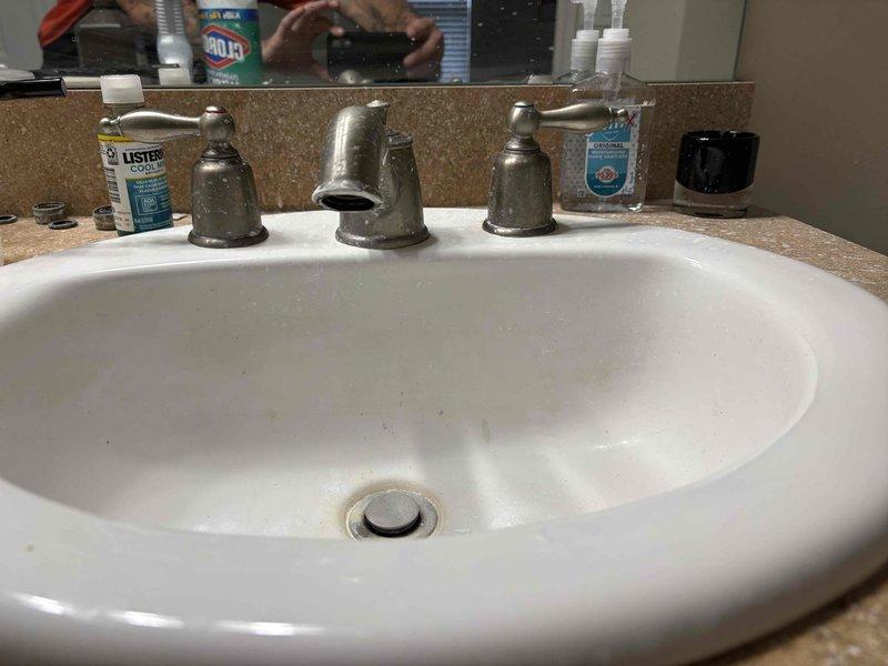 Completed follow-up plumbing repair service for bathroom vanity installation. Installed new three-piece chrome faucet set with separate hot and cold water handles and central spout on white oval drop-in sink with tan speckled countertop. All fixtures tested and confirmed operational with proper water flow and no leaks detected.