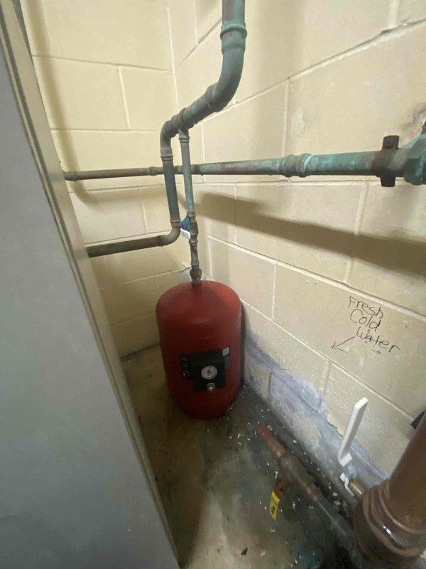 Completed installation of backflow prevention assembly and expansion tank in mechanical room utility space. The work included mounting a new pressure-rated backflow preventer (175 PSI rated) with dual isolation ball valves, installing a floor-mounted expansion tank with proper connections to the fresh cold water supply line, and addressing water pooling issues observed in the area. All components were secured according to plumbing code requirements with appropriate pipe supports and brackets.