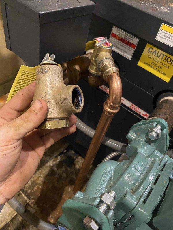 Returned to property to complete installation of pressure relief valve and expansion tank on hydronic heating system. Removed old expansion tank and associated fittings, then mounted new Amtrol expansion tank on existing wooden supports. Connected tank to system using copper piping and brass fittings, ensuring proper orientation and secure mounting. Installed new pressure relief valve with appropriate threaded connections to system piping. Verified all connections were tight and leak-free, checked system pressure on gauge, and confirmed proper operation of relief valve and expansion tank integration with existing circulator pump and controls.