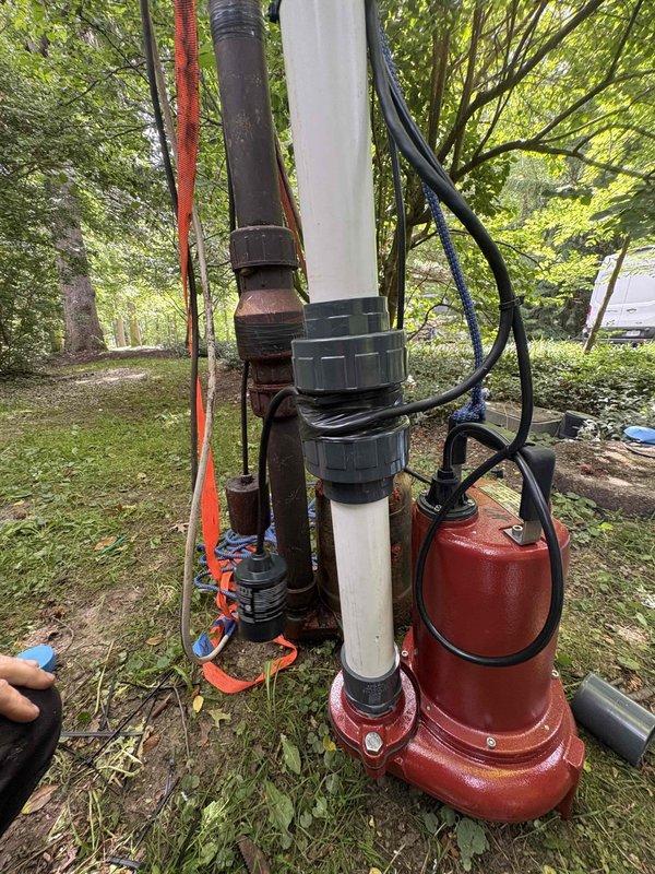 Returned to complete previously sold repair work involving a sump pump system installation in an outdoor drainage area. Replaced failed submersible pump with new red utility pump unit and reconstructed vertical discharge assembly using white PVC piping with appropriate union fittings and connectors. Removed deteriorated brown piping section and installed new plumbing configuration to effectively move water from natural stone-lined collection basin. Secured all electrical connections and routed power cord safely away from water contact points. System tested and confirmed operational for proper water removal from the wooded drainage site.