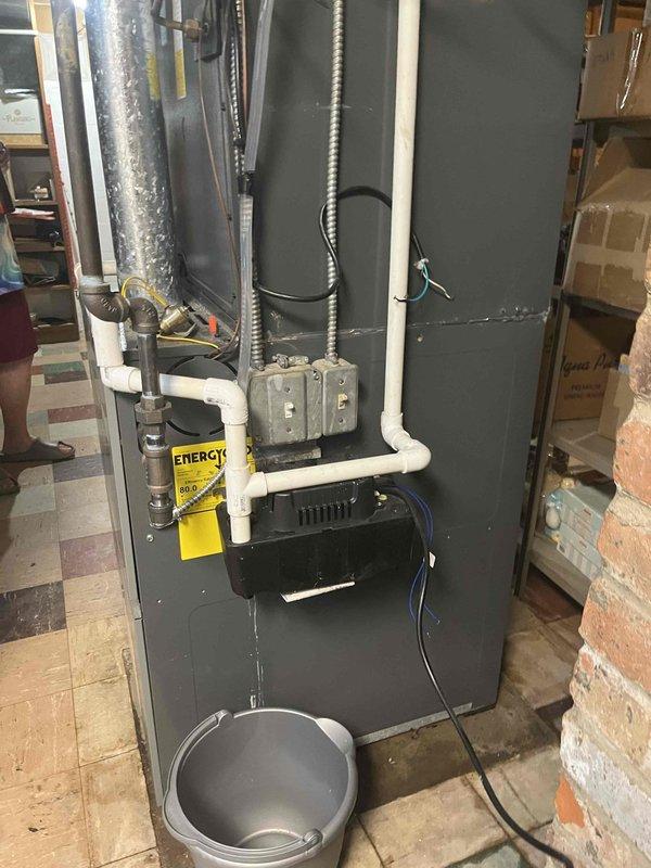 Responded to callback for recurring water leak from furnace. Upon arrival, inspected high-efficiency gas furnace unit and associated condensate drainage system including multiple PVC drain lines. Verified condensate pump operation and checked for blockages in drain lines and trap assembly. Bucket positioned at furnace base indicated active leak mitigation. Examined all pipe connections, seals, and drainage pathways to identify source of water intrusion. Documented equipment condition and drainage configuration for service records.