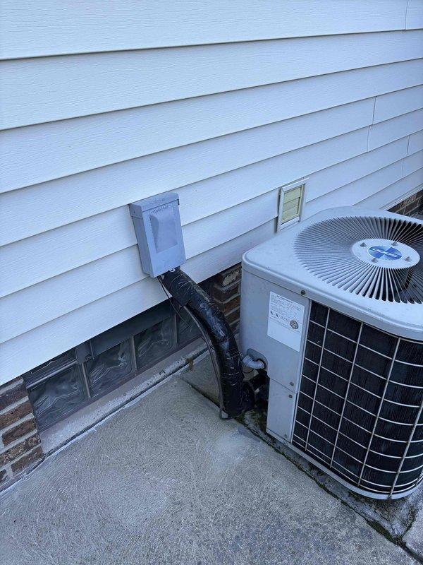 Conducted HVAC system evaluation for replacement estimate at residential property with rear driveway access. Assessed existing operational AC system with multiple units and current furnace setup. Customer requested quote for upgrading to high-efficiency 96% AFUE two-stage furnace with compatible air handler. Documented existing exterior condensing unit mounted on concrete pad against foundation, noting refrigerant lines and electrical connections to junction box on exterior wall. Inspected electrical panel to verify capacity and breaker configuration for proposed equipment installation. Photographed current HVAC equipment placement and electrical service to determine compatibility requirements for new high-efficiency system installation.