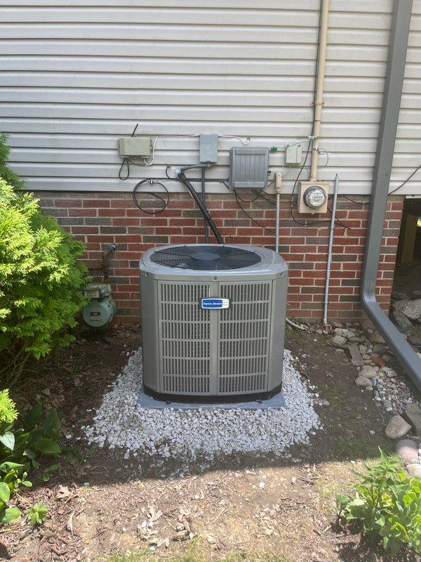 Completed full air conditioning system installation at residential property. New outdoor condenser unit was positioned on gravel pad against exterior wall with proper clearance for airflow and service access, connected to existing ductwork system. System startup and commissioning verified proper operation with temperature and humidity readings confirming adequate cooling performance.