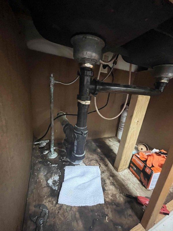 Responded to kitchen sink leak beneath cabinet. Upon inspection, found extensive water damage to cabinet floor with significant staining and deterioration from prolonged moisture exposure. Assessed plumbing assembly including garbage disposal unit, P-trap, and supply lines. Replaced deteriorated chrome piping and connections to eliminate active leak source. Cleaned and dried affected area, placing absorbent materials to address residual moisture. Tested all connections under pressure to verify proper seal and confirm leak resolution.